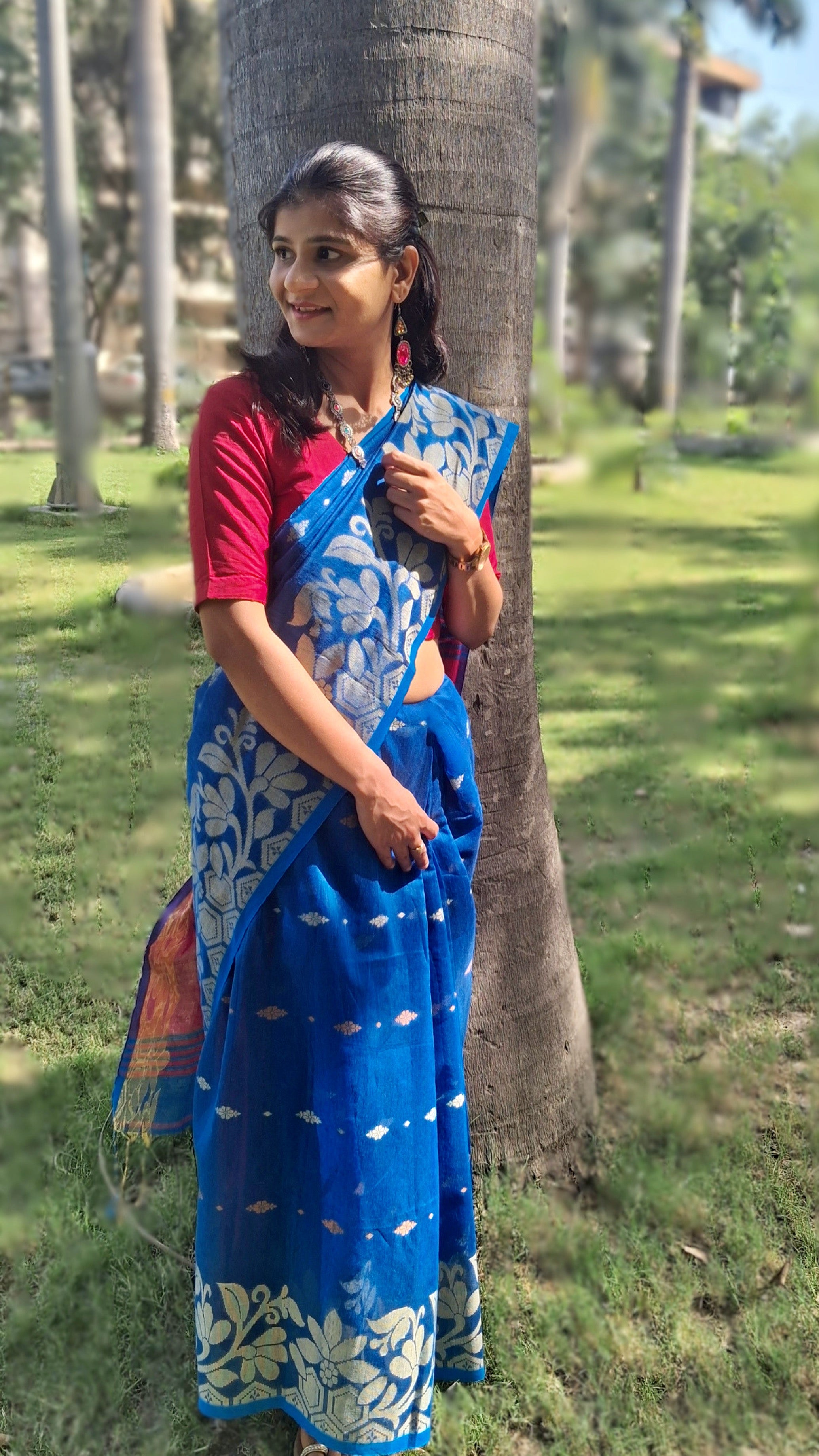 Left view of a handwoven blue Shantipuri Tant saree with woven motifs and a contrasting red pallu.